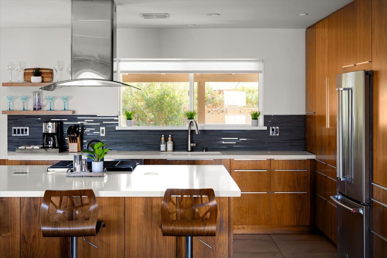 A modern kitchen with a large island, wooden cabinets, stainless steel appliances, and a window providing natural light.