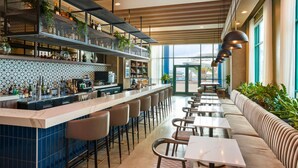 Uma área de bar com um balcão extenso, diversas opções de assento e vista através de grandes janelas.