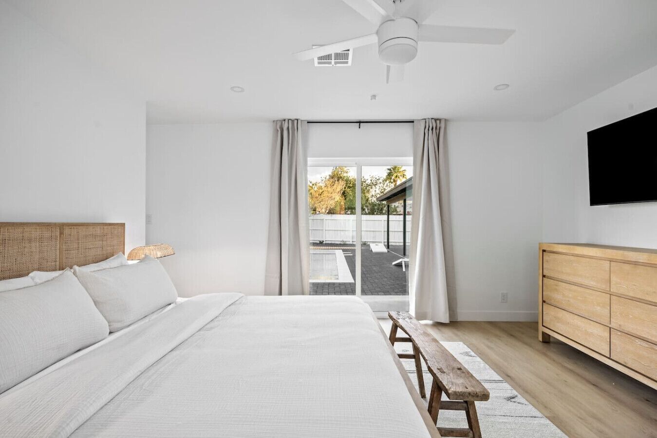 Une chambre à coucher moderne avec un grand lit, un banc en bois, une commode en bois et un ventilateur de plafond.