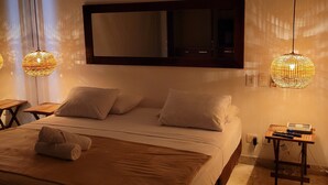 Un dormitorio con una cama grande, dos mesitas de noche, un ventilador de techo y lámparas colgantes.