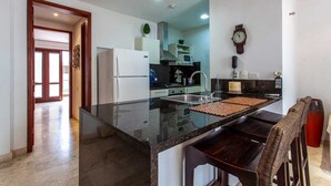 Una cocina moderna con encimera negra, electrodomésticos de acero inoxidable y una silla de madera.