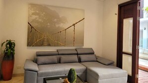 Una sala de estar moderna con un sofá modular gris, un ventilador de techo, un cuadro abstracto grande y una planta en maceta.