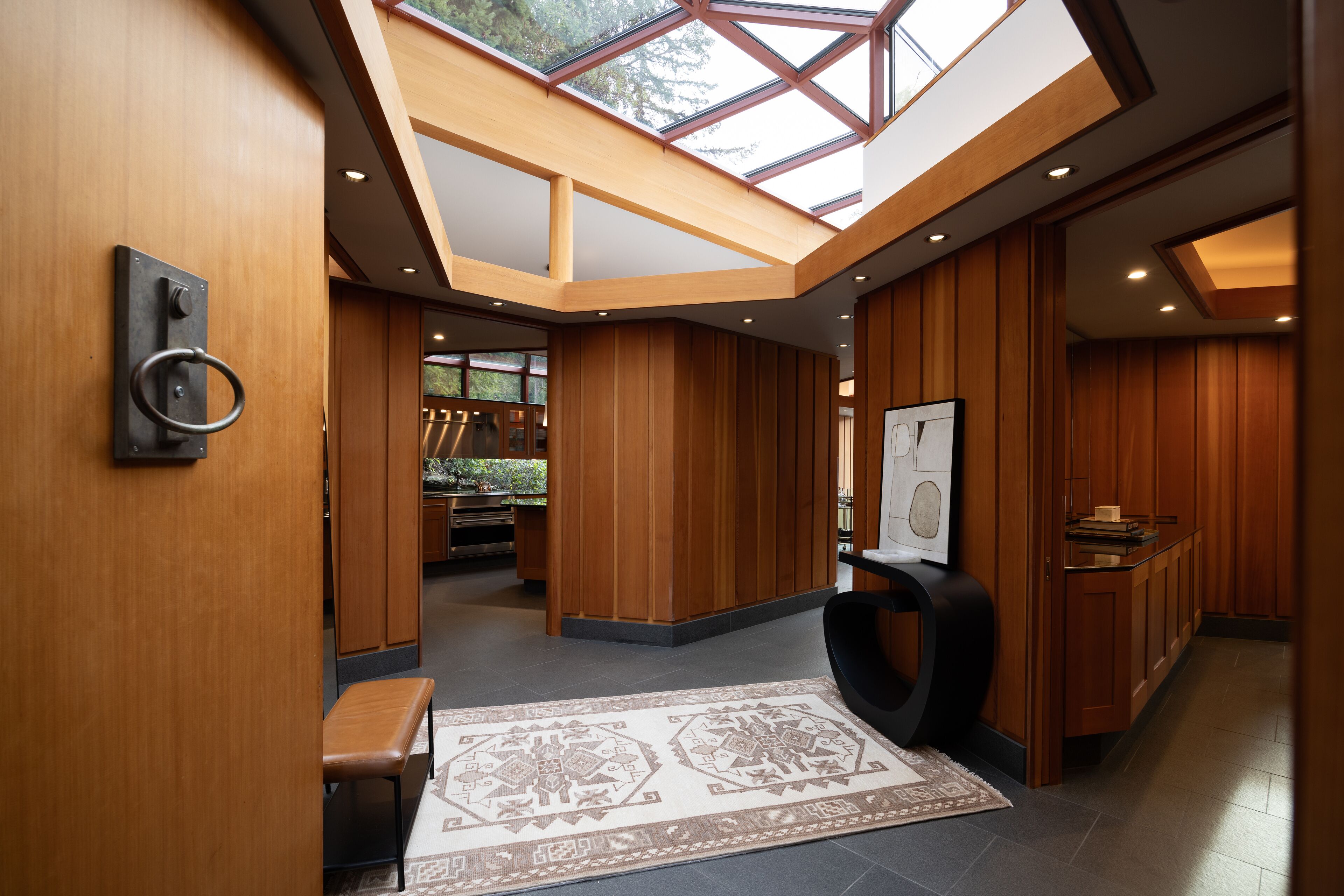 Een modern interieur met houten lambrisering, een dakraam, een bank en een vloerkleed.