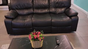 Ein Wohnzimmer mit einer schwarzen Ledersofa, einem schwarzen Marmortisch mit einer Blumenkorb und einem gerahmten Bild von einem Baum an der Wand.