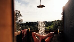 A hand under a showerhead with water flowing into a basin, overlooking a landscape with trees and hills.
