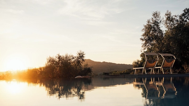 A serene pool area with lounge chairs and a clear view of the sunset over a hilly landscape.