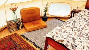 A cozy tent interior with a cushioned seating area, a small table with a vase, a potted plant, and a bed with patterned bedding.