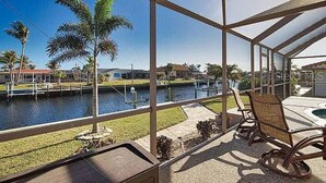 Ein überdachter Patio mit Blick auf ein Gewässer und Palmen.