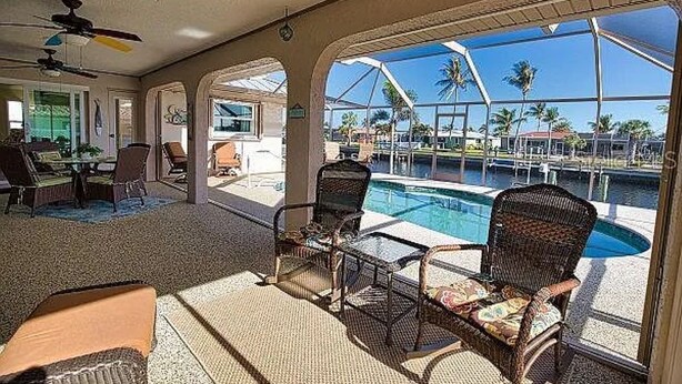 Ein Poolbereich mit Korbstühlen und einem Glastisch, mit Blick auf einen Pool und Palmen.