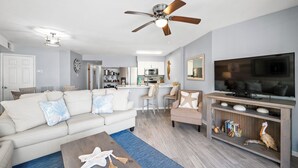 A modern living room with a sofa, coffee table, TV stand, and a ceiling fan. - ☀Sundazed☀ ~ Spectacular Beachside Condo w/Fabulous Pool at Tradewinds in OBA⛱ (Orange Beach)