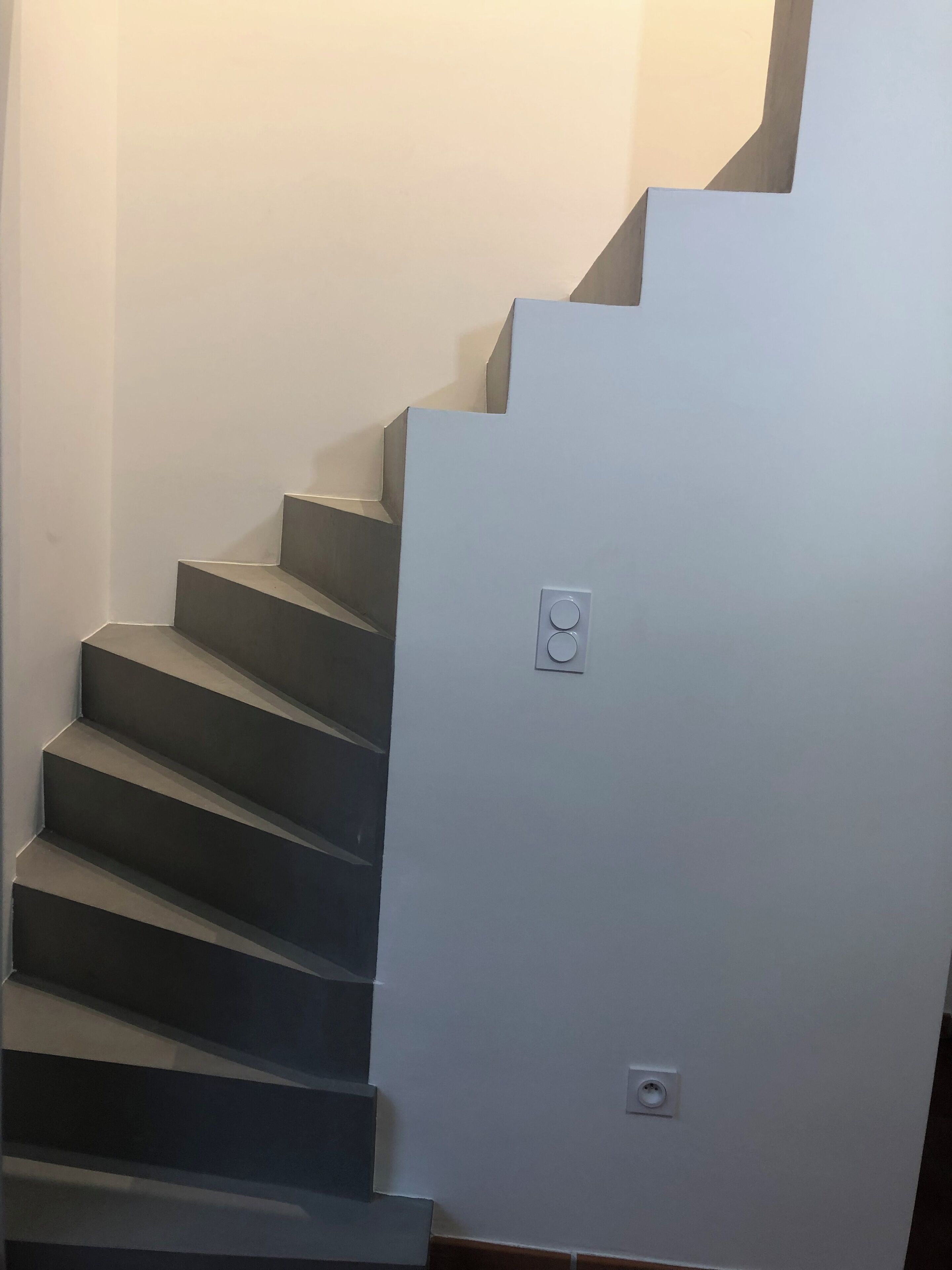 Een moderne trap met een lichtgekleurde muur en een stopcontact op de overloop.