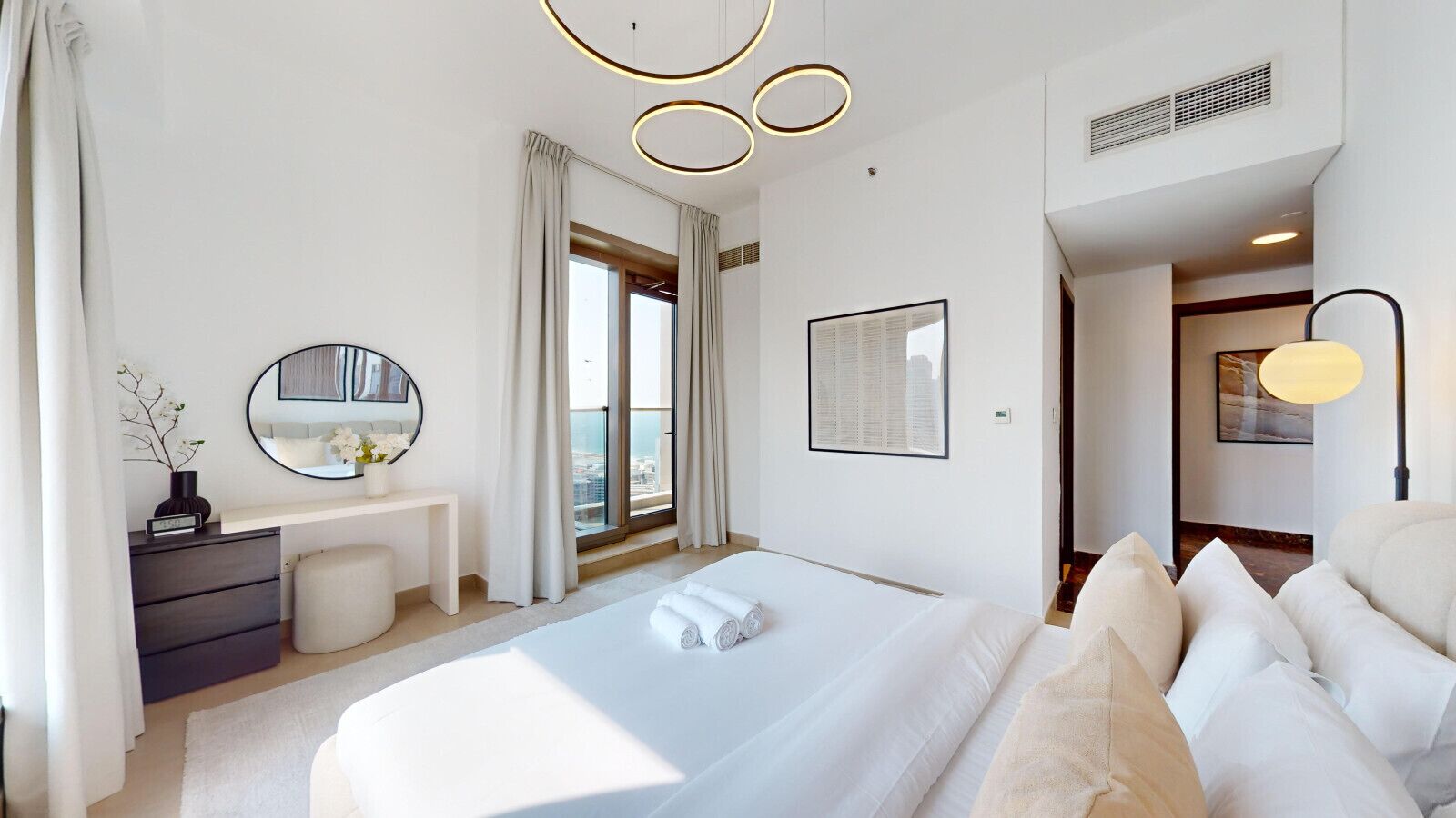 Une chambre d’hôtel moderne, dotée d’un grand lit, d’un bureau, d’un miroir et offrant une vue sur la ville par la fenêtre.