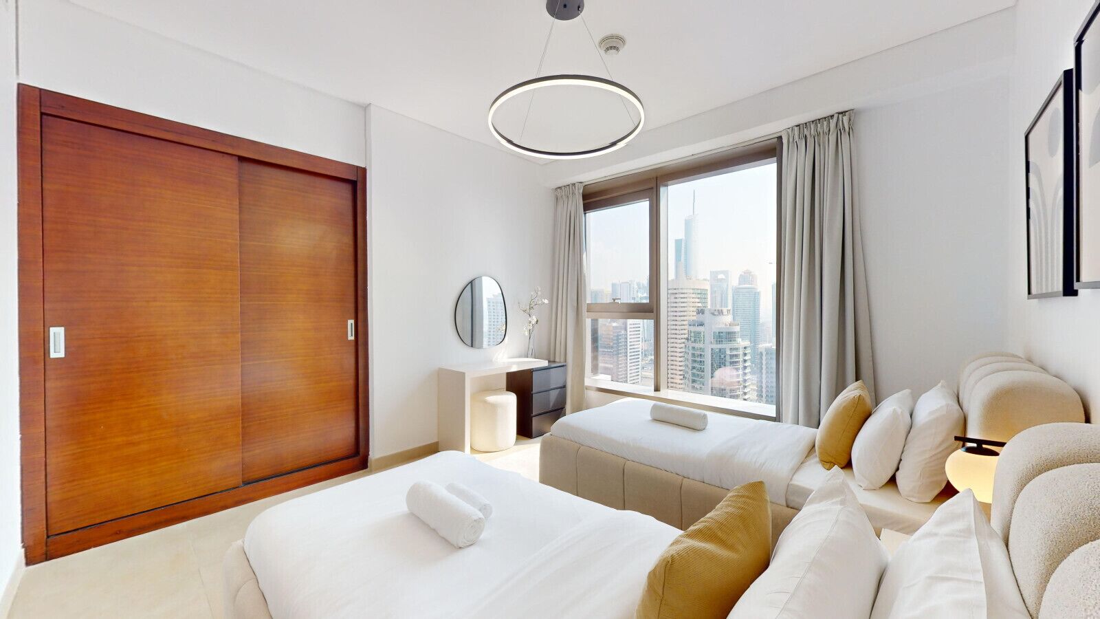 Ein modernes Hotelzimmer mit großem Kleiderschrank, einem Bett mit weißer Bettwäsche, einem Nachttisch mit Lampe und Blick auf die Stadtkulisse durch große Fenster.