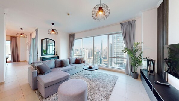 A modern living room with a grey sectional sofa, a round coffee table, and a large window offering a city view.