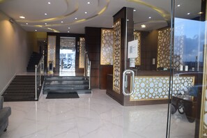 A hotel lobby with a reception desk, a staircase, and a glass partition.