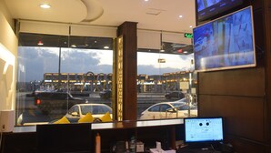 Een hotellobby met een groot raam dat uitzicht geeft op de straat. Er zijn meerdere schermen waarop beveiligingsbeelden te zien zijn.
