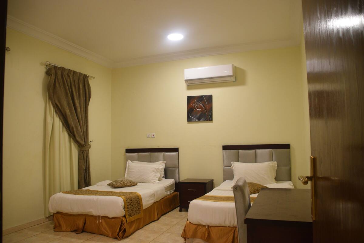 A hotel room with two beds, a nightstand, an air conditioner, and a door.