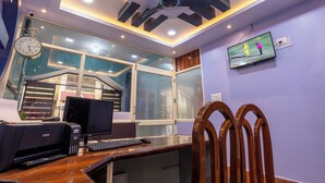 A modern office with a ceiling fan, a clock, a computer setup, and a TV on the wall.