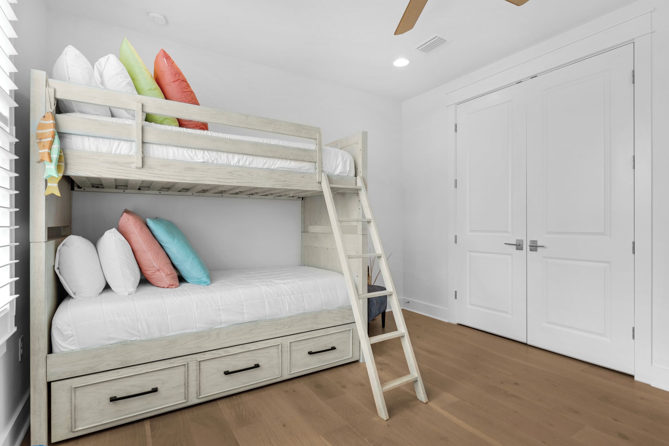 Una cama litera con escalera, paredes blancas y suelo de madera.