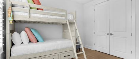 Una cama litera con escalera, paredes blancas y suelo de madera.