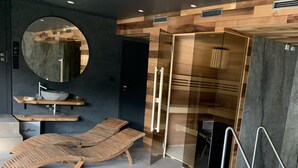 Un baño moderno con tocador de madera, un espejo redondo, cabina de ducha con paredes de vidrio y una tumbona.