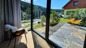 Una habitación con un amplio ventanal que ofrece vistas a un patio de piedra, mobiliario exterior y un edificio de madera.