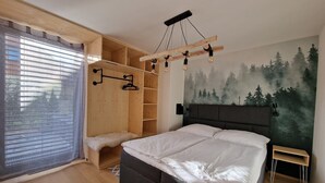 Un dormitorio con una cama, un armario de madera, un banco y un mural con motivos de bosque en la pared.