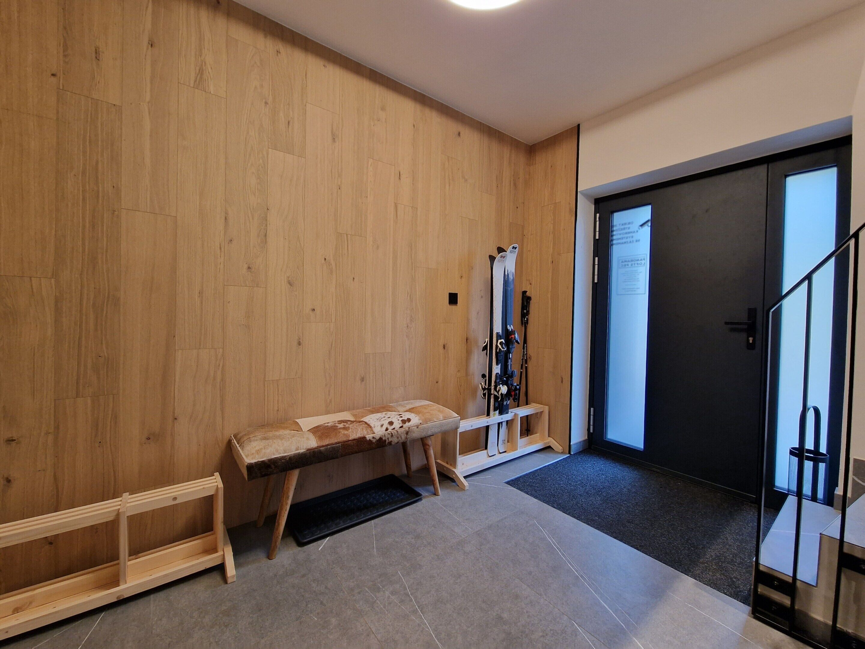 A wooden room with a bench, skis, and a door.
