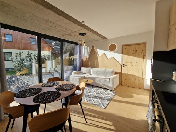 A modern living room with a dining area, a sofa, a TV, and a kitchen area.