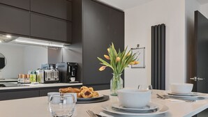 A modern kitchen with dark cabinets, a coffee machine, a toaster, and a vase with flowers on the counter.
