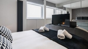 A modern hotel room with a large bed, a flat-screen TV, a mirror, and a window.