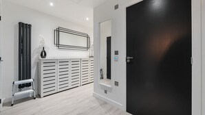 A modern hallway with a black door, a white wall with a framed artwork, and a white console with drawers.