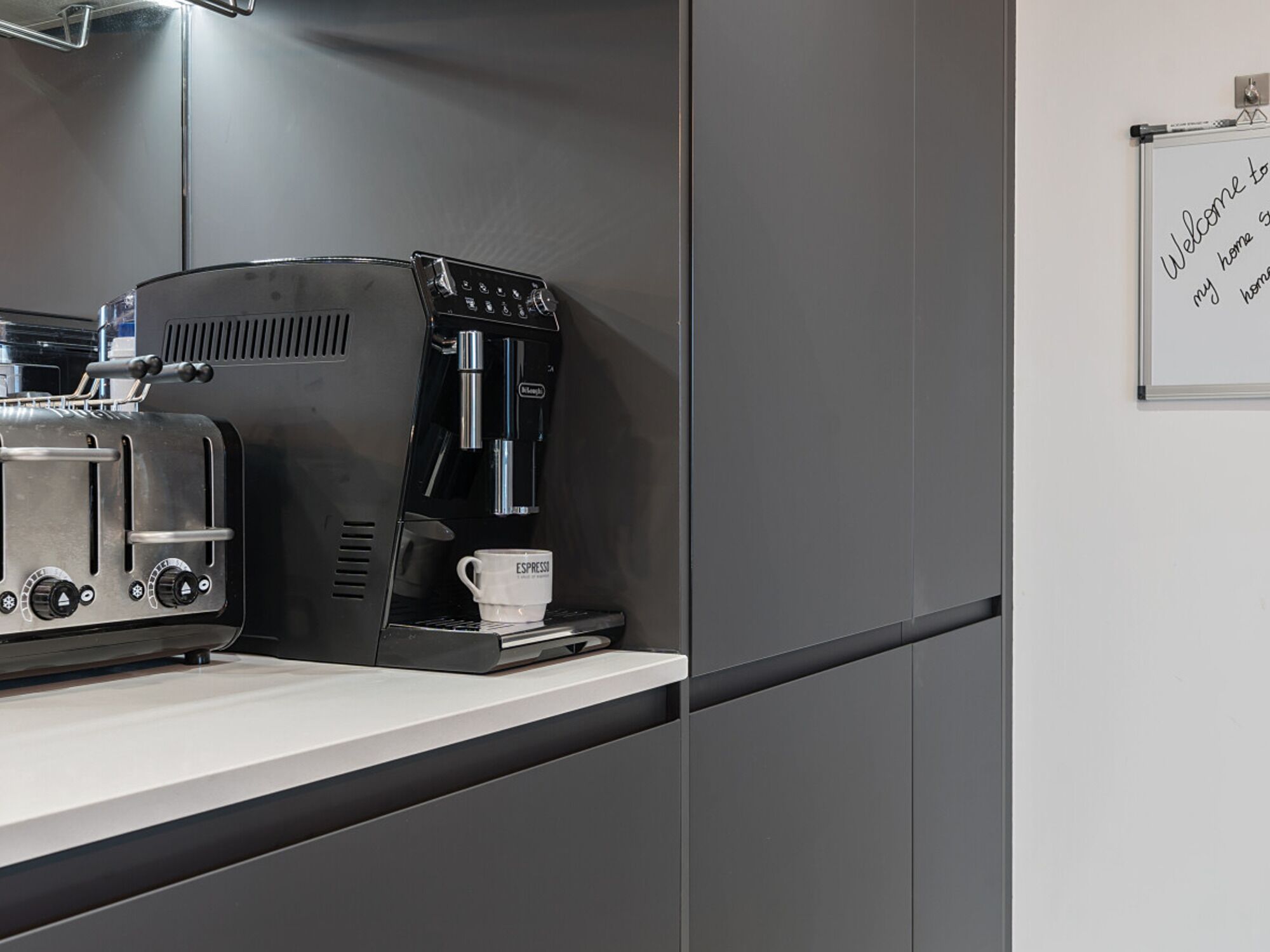 Eine Küchenzeile mit Kaffeemaschine, Toaster und einer weißen Tasse auf der Arbeitsfläche.