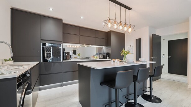 A modern kitchen with dark cabinetry, a central island with bar stools, a built-in oven, and a pendant light fixture.