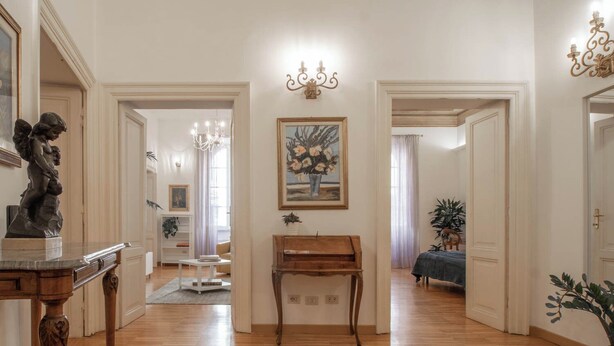 A spacious hallway with wooden flooring, a piano, and a statue on the left. There are doors leading to other rooms, and a chandelier hangs from the ceiling. - NICALANDRO HOUSE - ROME CENTER (Roma)