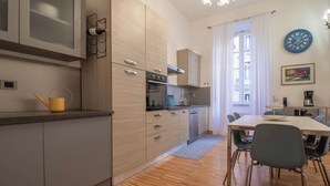 A modern kitchen with wooden cabinets, a dining area with a table and chairs, and a clock on the wall. - NICALANDRO HOUSE - ROME CENTER (Roma)