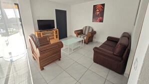 A living room with a sofa, a wooden coffee table, a TV on a stand, and a chair. - villa sophie glamour beach (Nosy Be)