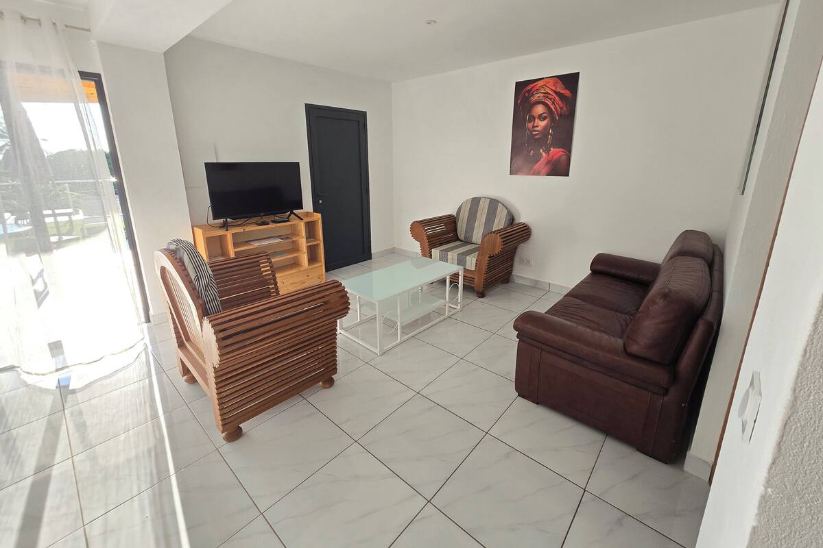 Uma sala de estar com um sofá, uma mesa de centro de madeira, uma TV em um suporte e uma poltrona.