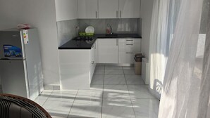 A compact kitchen with white cabinets, a black countertop, and a refrigerator. - villa sophie glamour beach (Nosy Be)