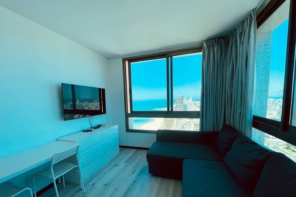 A modern living room with a large window, a flat-screen TV, a sofa, and a desk.