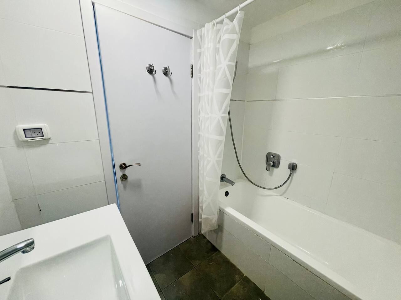 Een badkamer met een witte badkuip, een douche met gordijn, een wastafel en een deur.