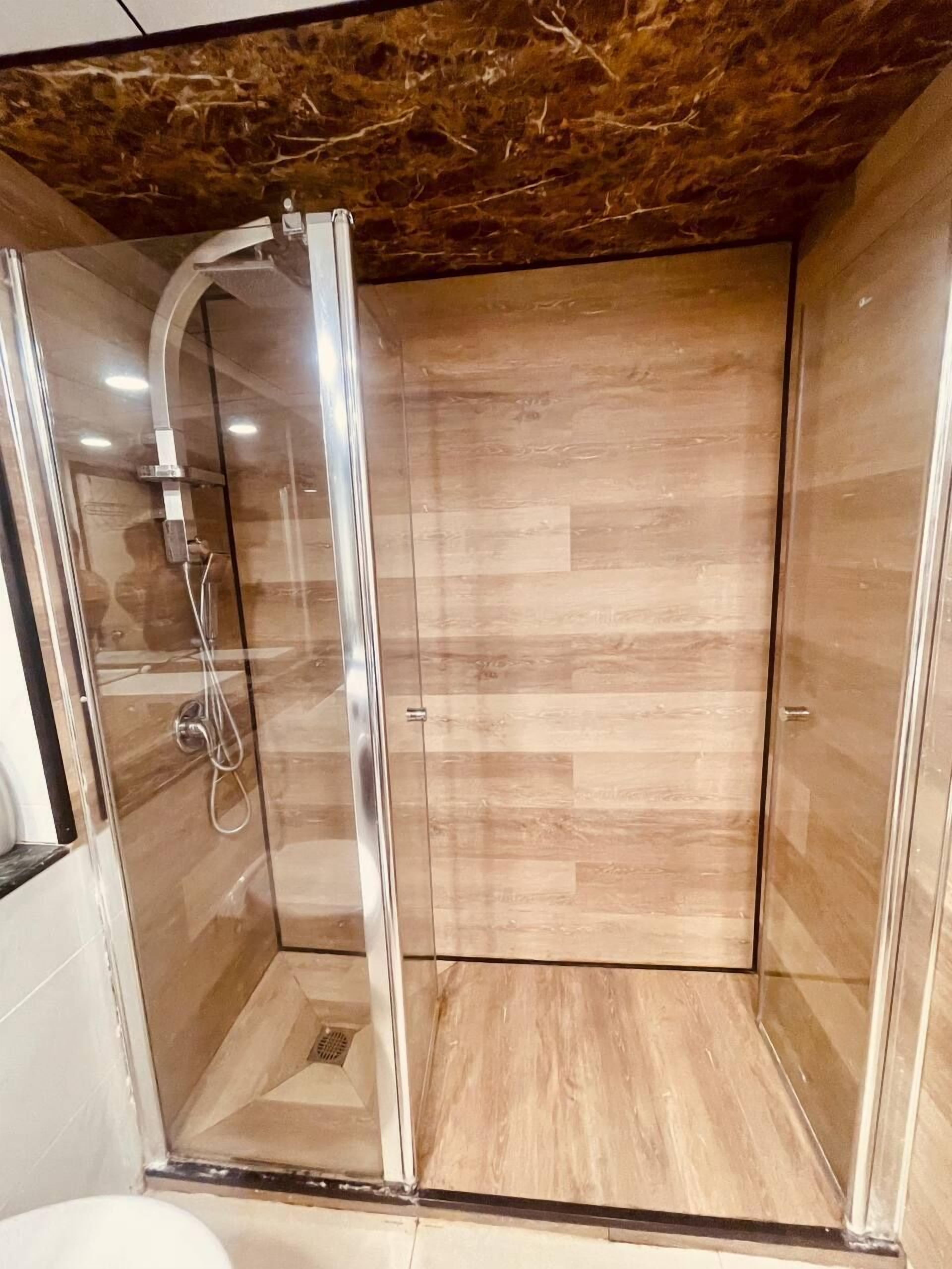 Ducha con cerramiento de vidrio, suelo de madera y techo de mármol.