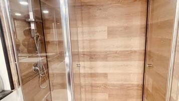 Ducha con cerramiento de vidrio, suelo de madera y techo de mármol.