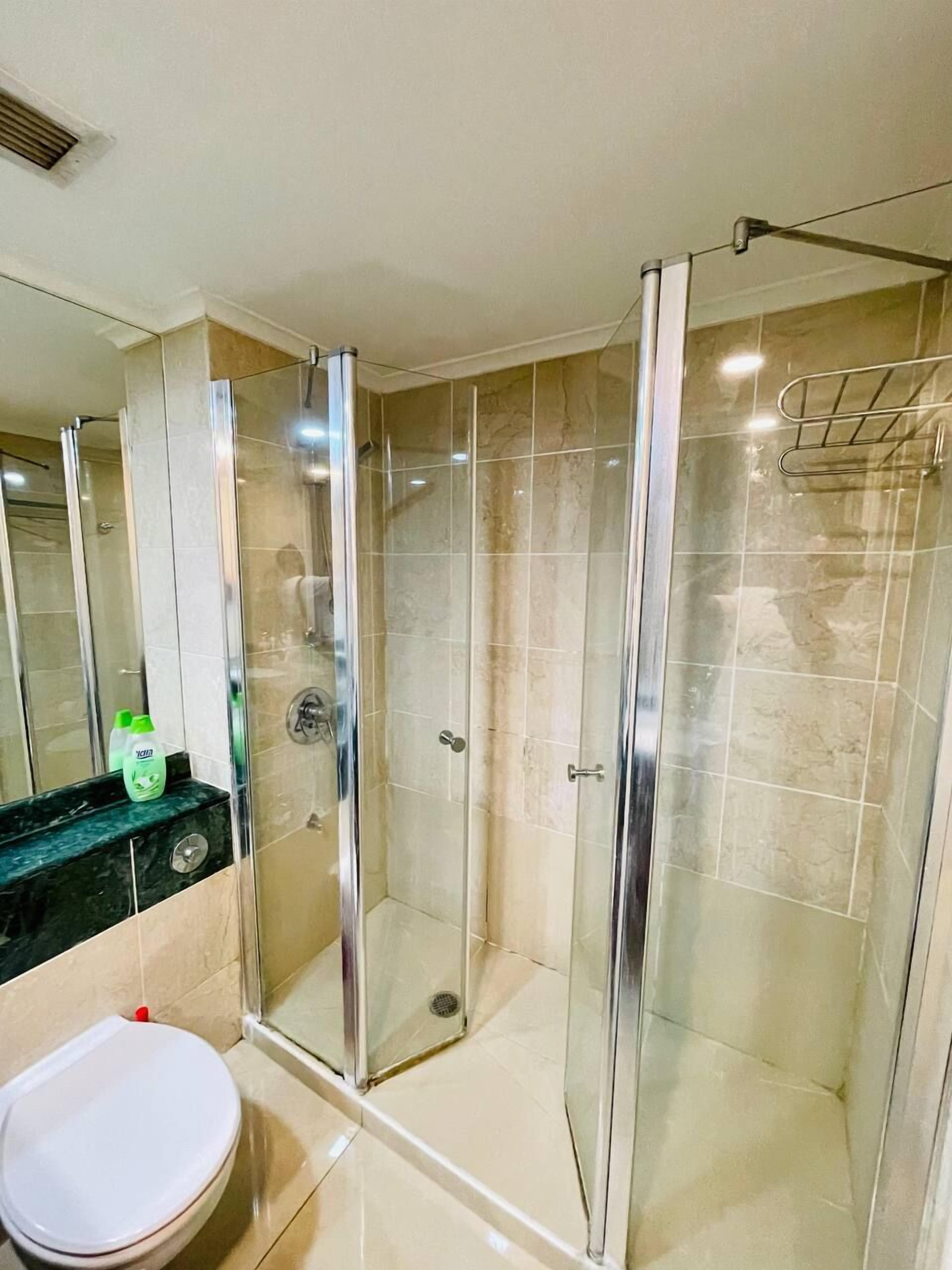 A modern bathroom with a glass-enclosed shower, a white toilet, and a black countertop with a soap dispenser.