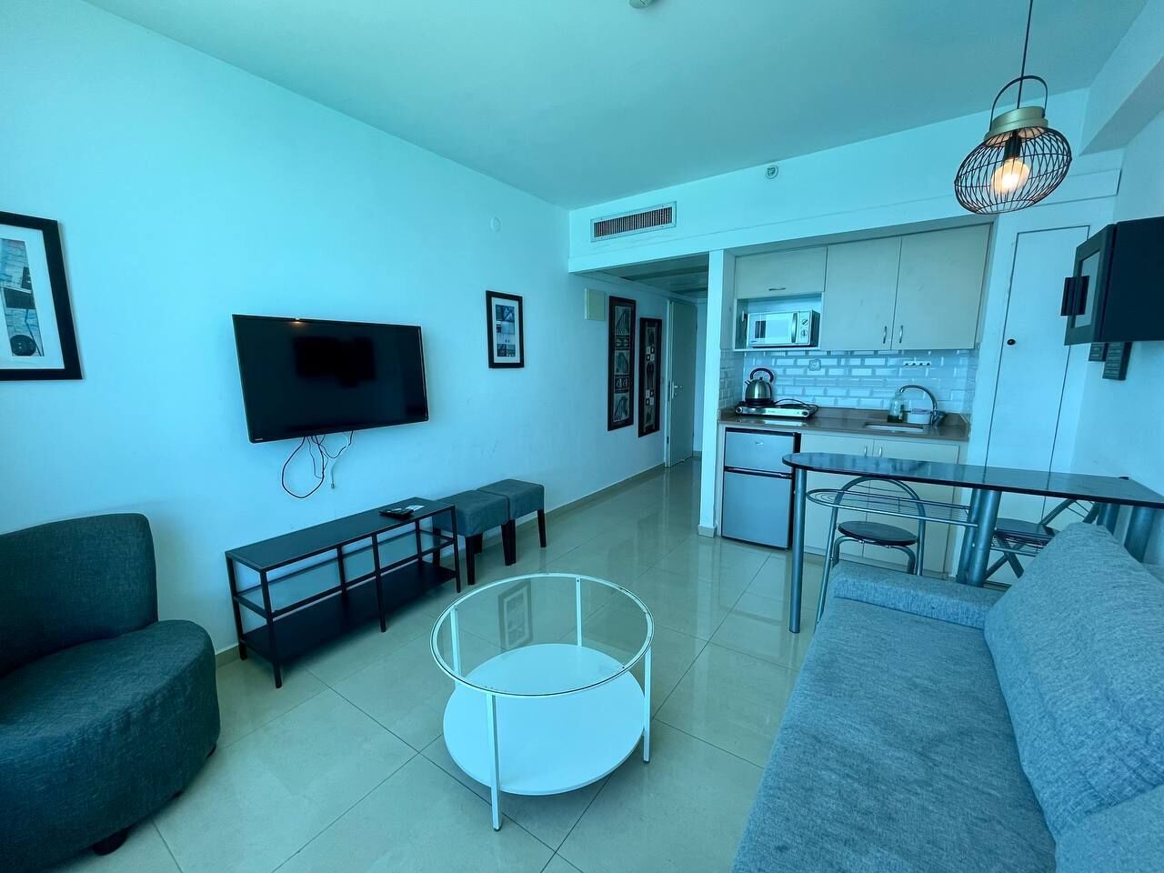 Un soggiorno moderno con una TV a schermo piatto, un divano grigio, un tavolino in vetro e un'area pranzo con una cucina sullo sfondo.