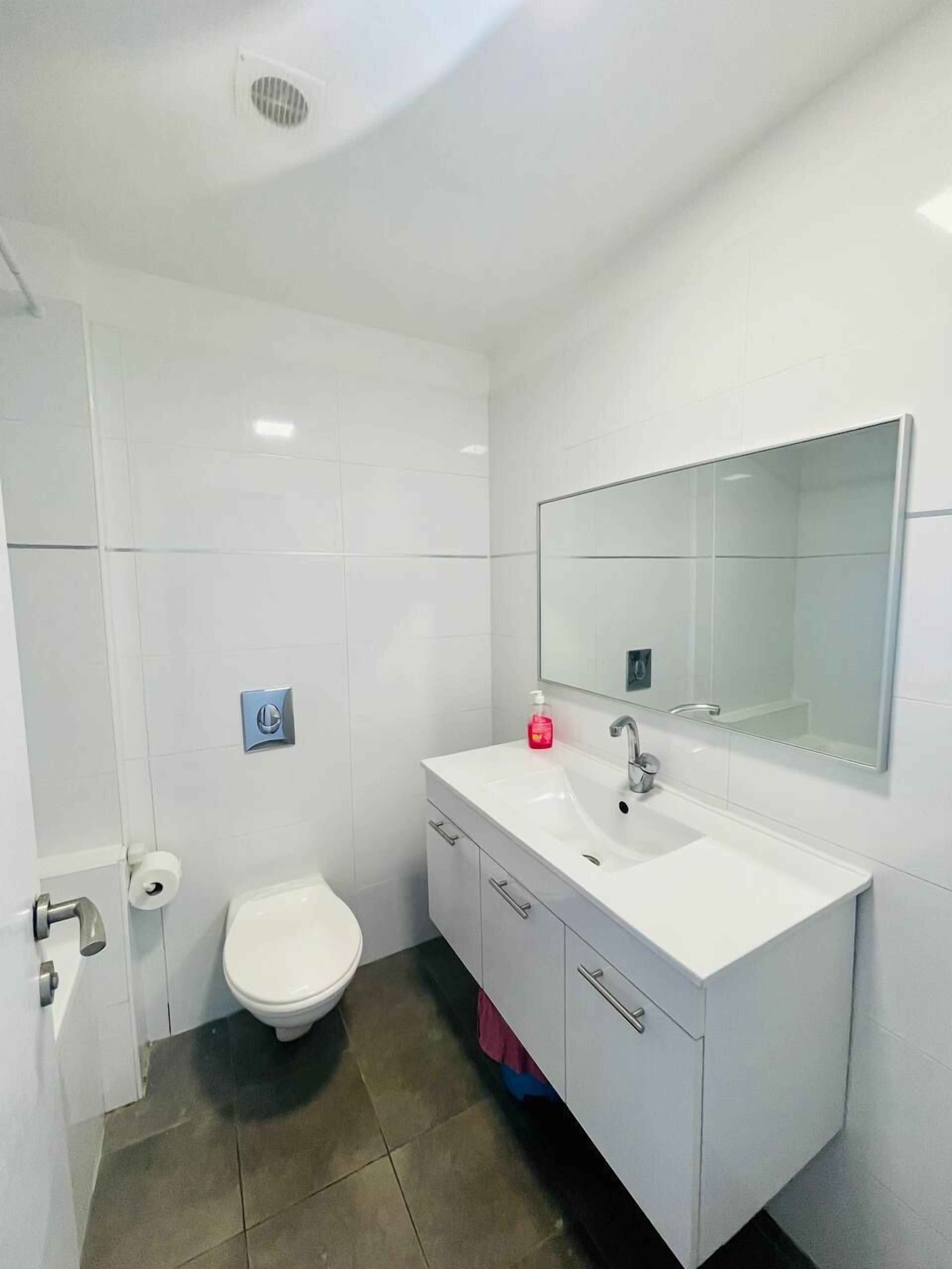A modern bathroom with a white sink, mirror, and toilet.