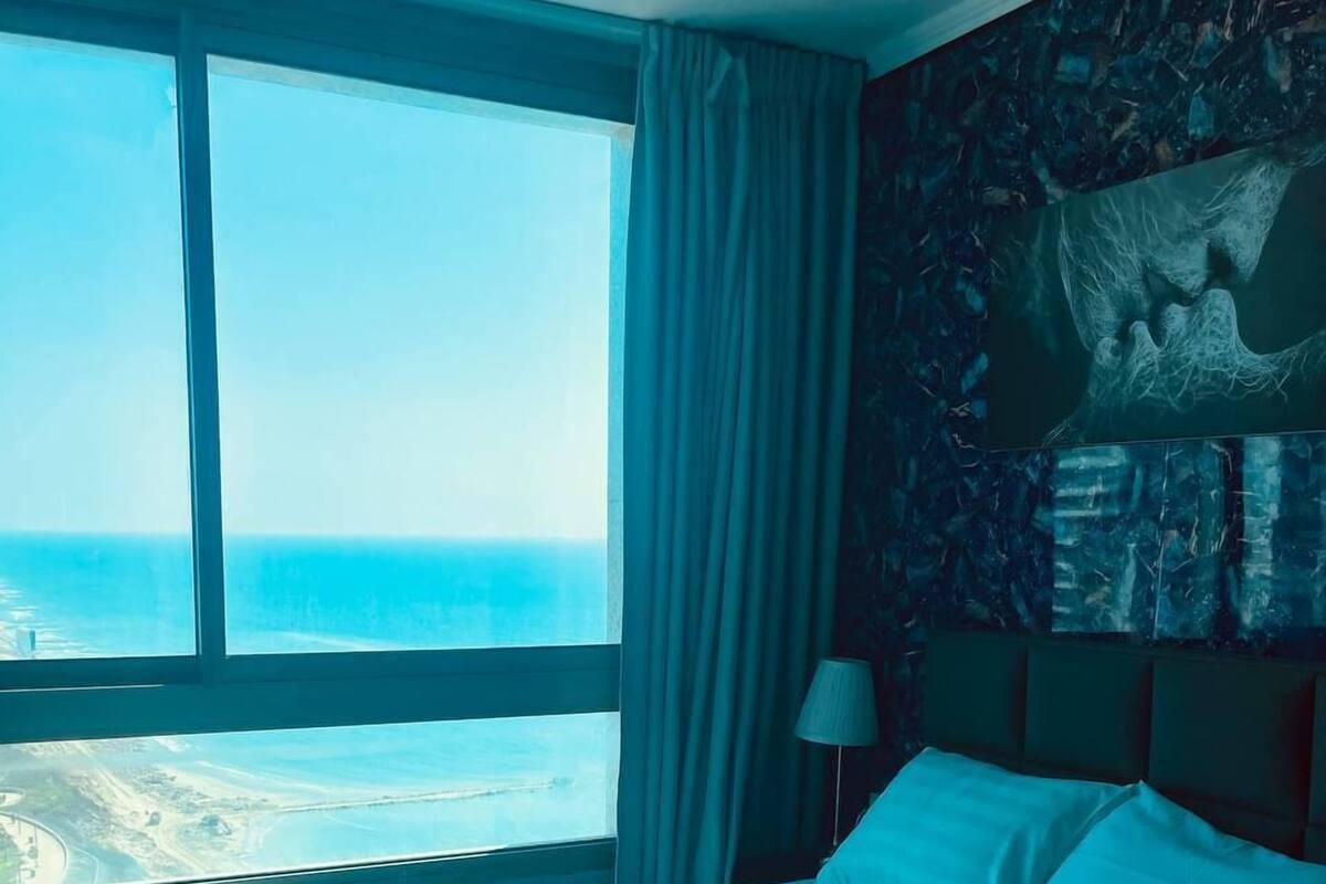 A hotel room with a large bed, a view of the ocean, and a mural on the wall.