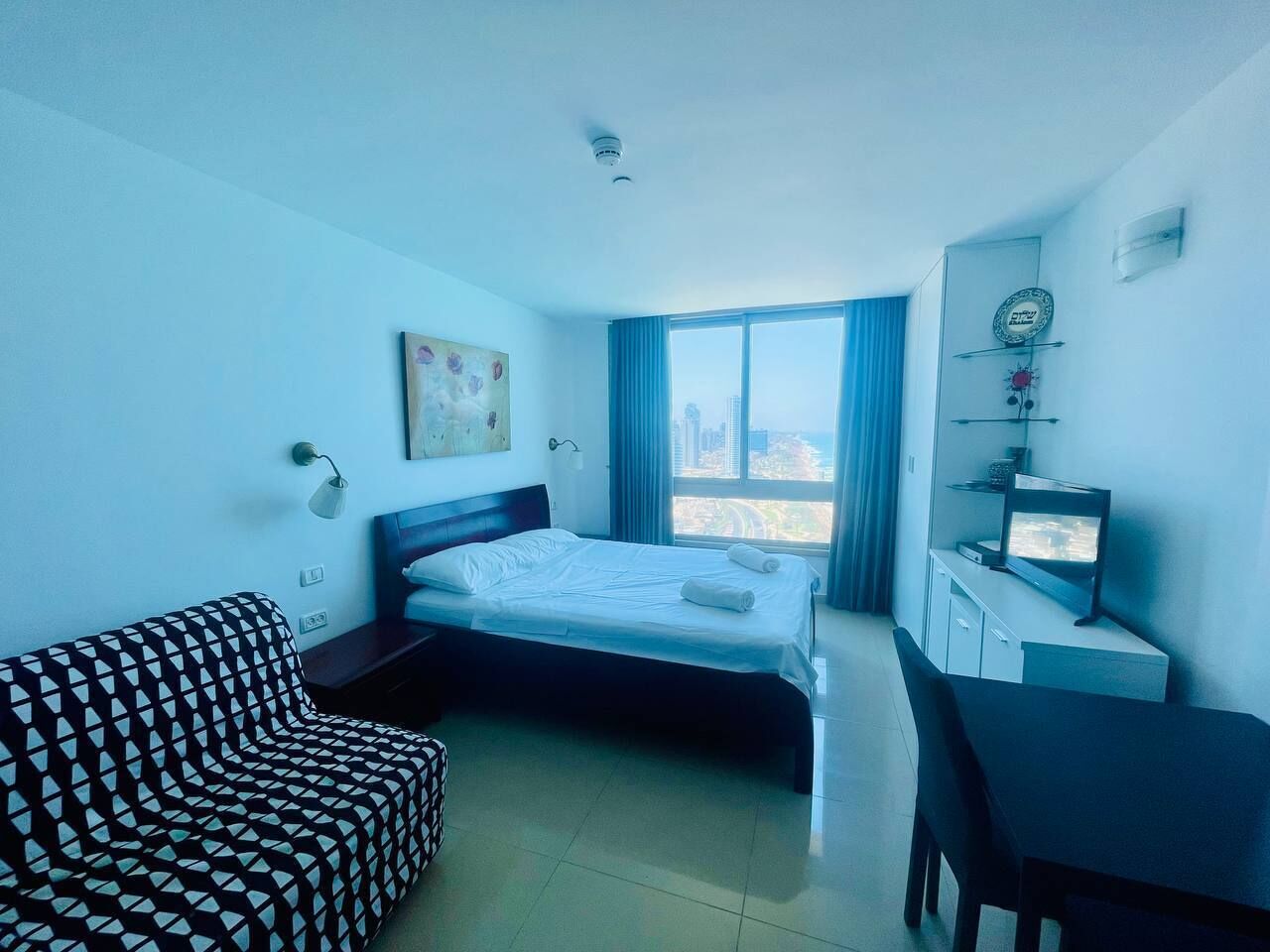 A hotel room with a bed, a sofa, a desk, and a television.