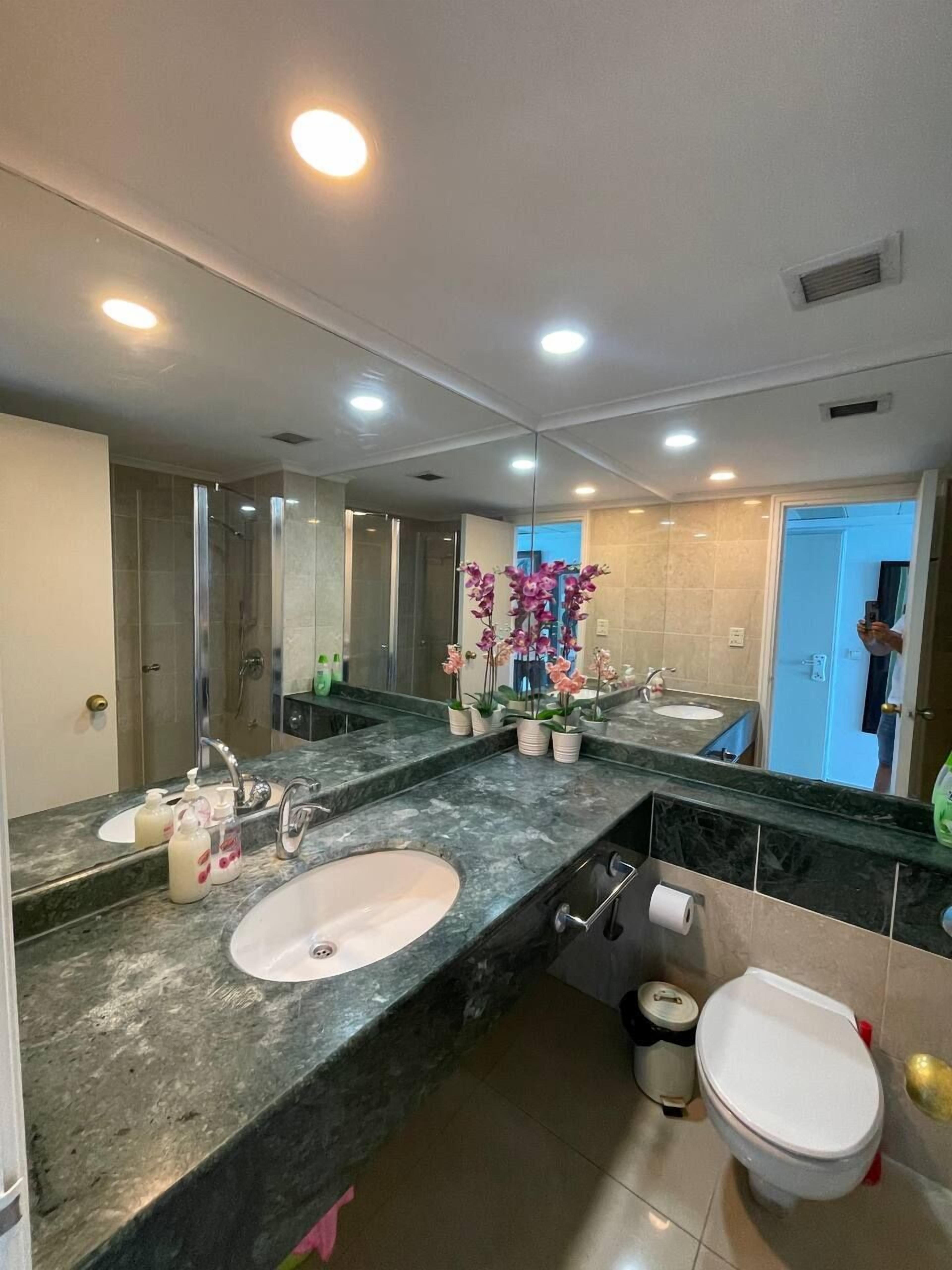 Une salle de bain moderne avec un grand miroir, deux lavabos, des toilettes et une douche.