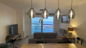 A modern living room with a large window, a dining table, and a TV. - Apartment Near Marina Nieuwpoort & Golf (Nieuwpoort)